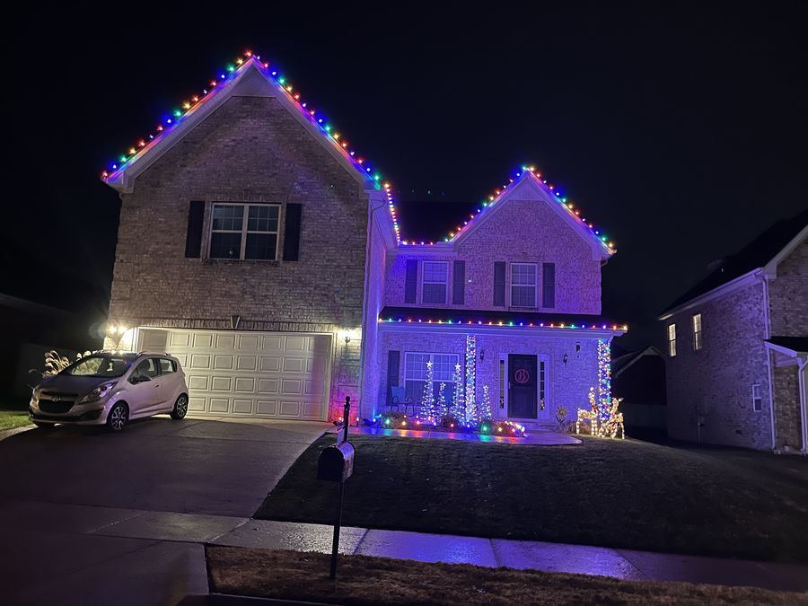 Two-story home at dusk with multicolor lights on the roofline and porch