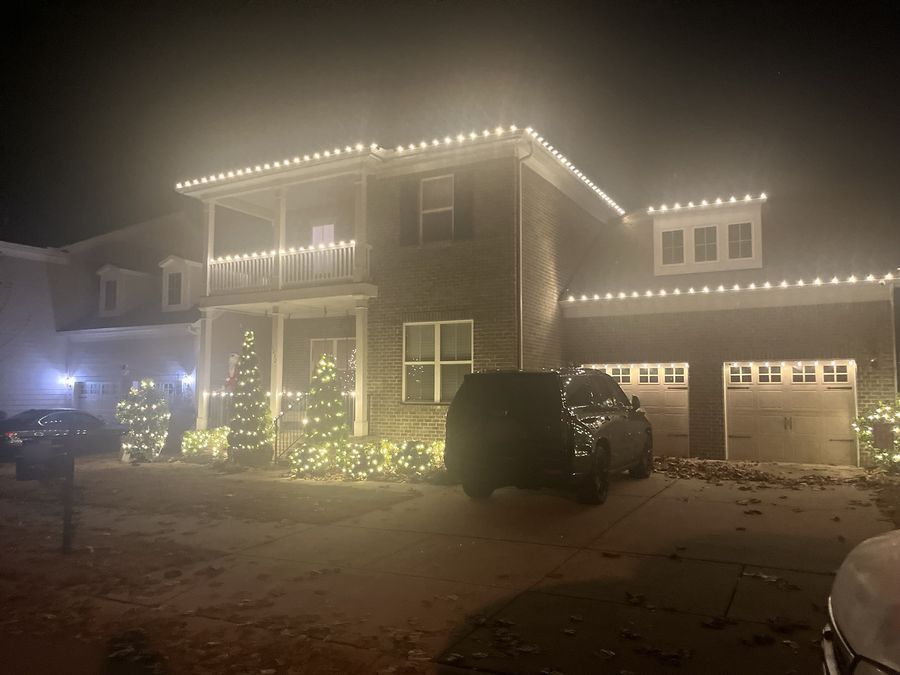 Brick home with multicolor roofline lights and lit yard decorations