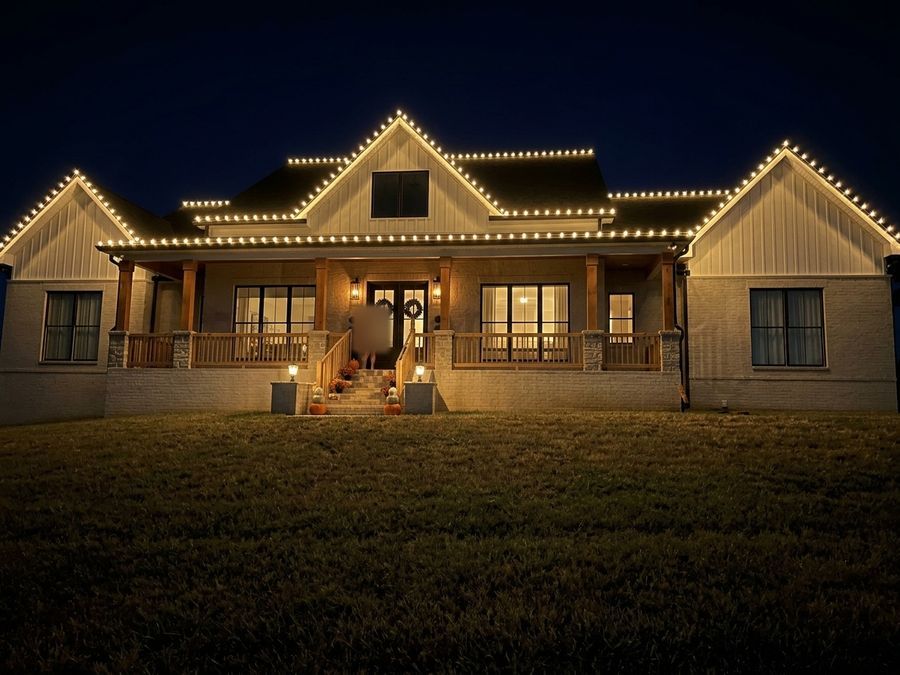 Ranch home with a wraparound porch outlined in warm white Christmas lights