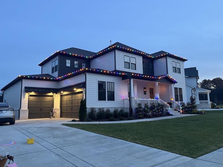 Brick home with warm white roofline lights and wrapped landscaping